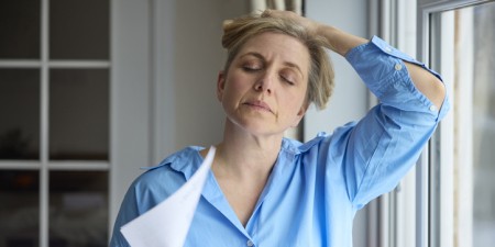 Menopausal Mature Woman Having Hot Flush At Home Cooling Herself With Letters Or Documents